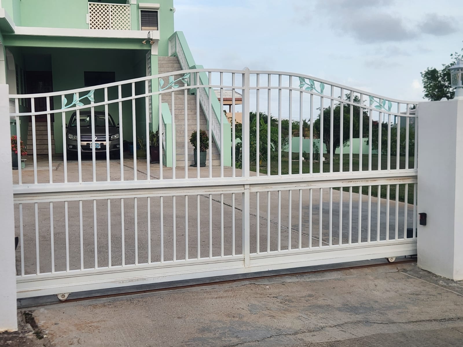 White aluminium sliding driveway gate with cut leaf and vine detailing at a home in Anguilla