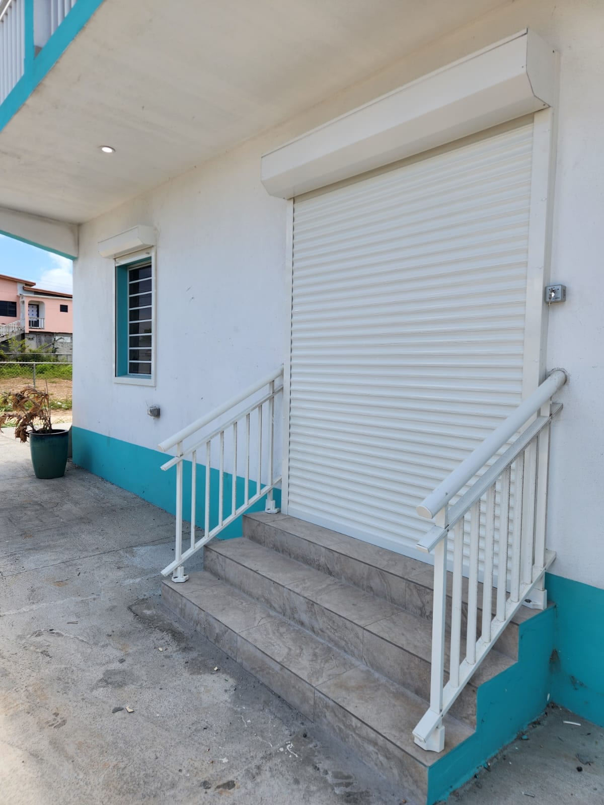 Closed white roller shutter beside tiled steps with a white aluminium handrail in Anguilla